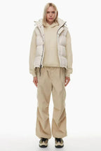 Full body shot of a woman in a cream puffer vest, cream hoodie, and tan cargo pants