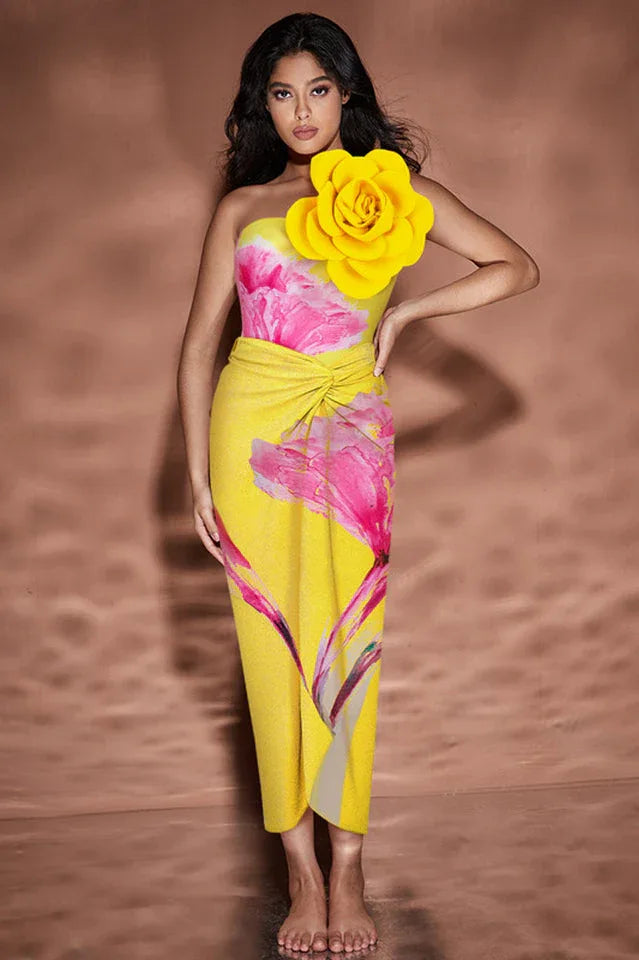 Woman in yellow one-piece swimsuit with floral print and large yellow flower embellishment on shoulder, standing with hand on hip. Main image