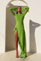 Woman wearing a lime green metallic knit dress with an asymmetrical ruffled hemline and an open back, posing with hands behind her head.