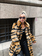 A woman with blonde hair styled in a bun, wearing a faux fur tiger stripe coat and sunglasses, outdoors.