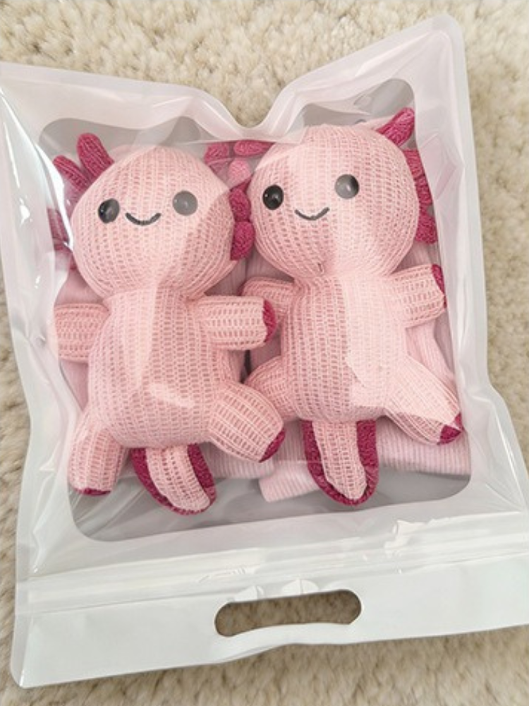 A pair of light pink ribbed socks with pink axolotl appliques are packaged in a clear plastic bag.