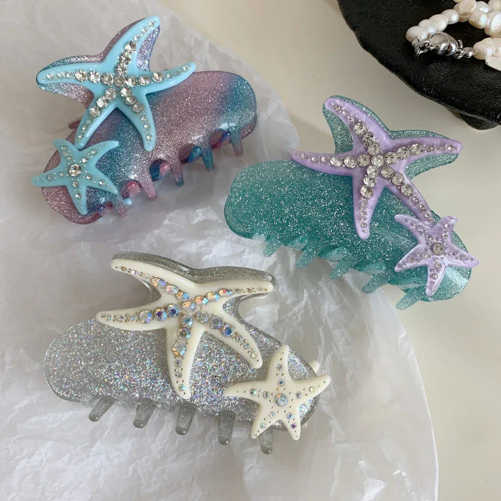 Three glitter hair claw clips with starfish and rhinestone embellishments in blue/pink, purple/teal, and silver/white colorways.