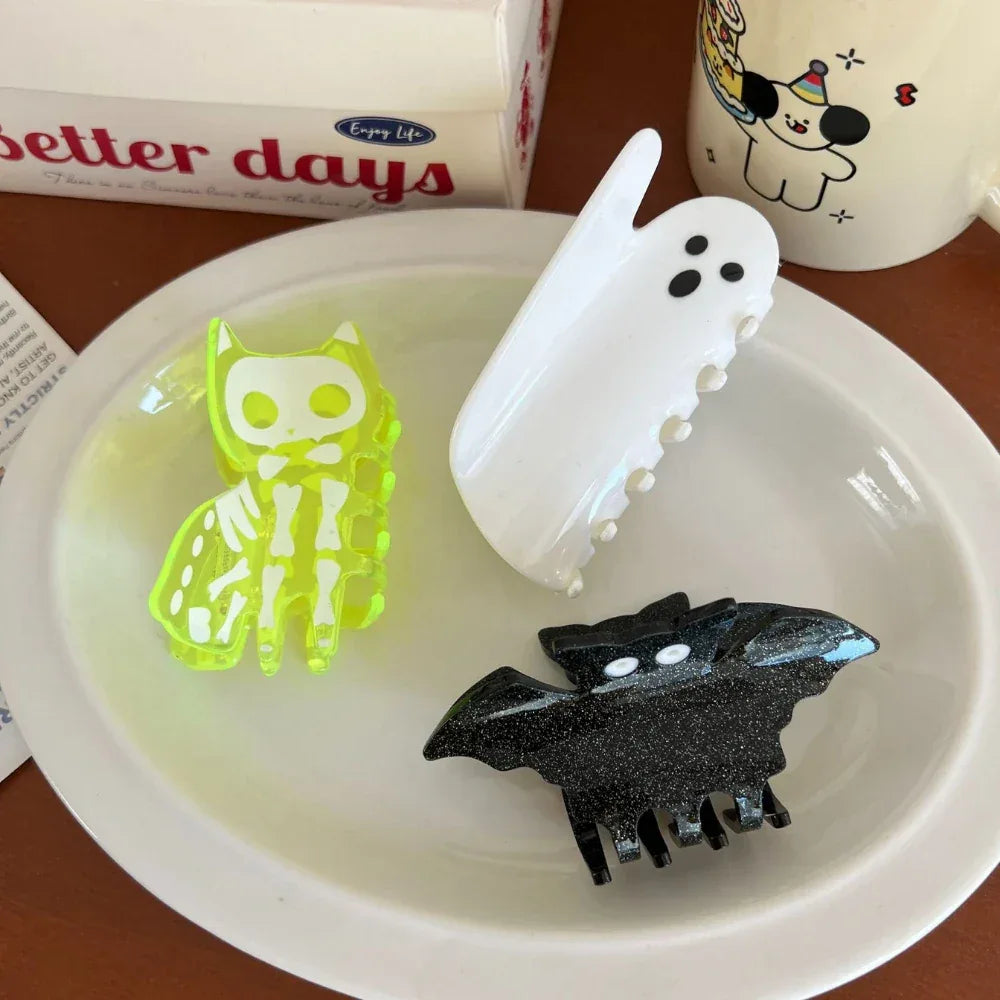 Three Halloween hair clips: skeleton cat, ghost, and bat, arranged on a plate