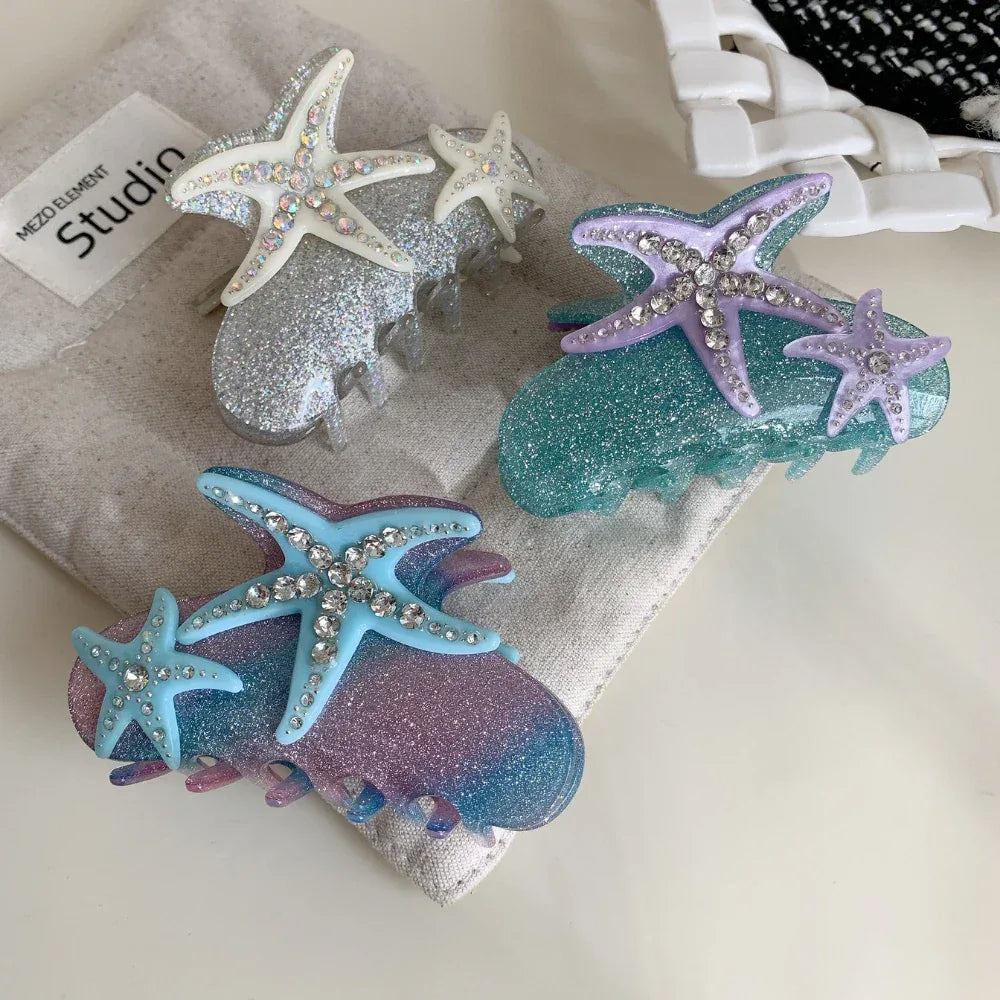 A close-up of three seashell-themed glitter hair claw clips, each adorned with two sparkling starfish.