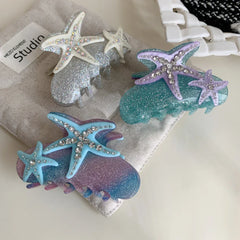 A close-up of three seashell-themed glitter hair claw clips, each adorned with two sparkling starfish.