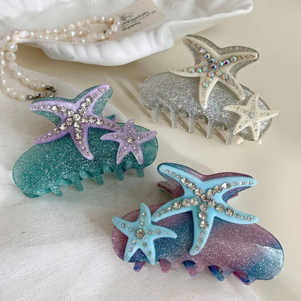 A collection of three sparkling hair claw clips, each featuring two starfish charms with crystal accents and a gradient glitter base in ocean-inspired colors.
