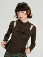 Front view of a model wearing a brown long-sleeved ribbed top with cut-out shoulders and a lace-up detail, holding the lace strings.