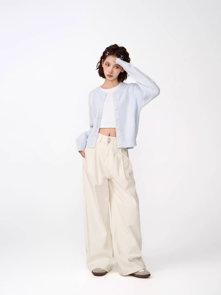 Woman posing with hand on forehead, wearing a light blue cropped knit cardigan, white crop top, and cream wide-leg pants.