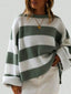 Woman wearing a green and white striped knit sweater with rolled-up sleeves and a gold pendant necklace, paired with white bottoms.
