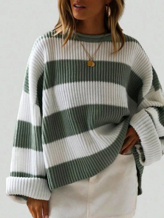 Woman wearing a green and white striped knit sweater with rolled-up sleeves and a gold pendant necklace, paired with white bottoms.