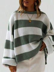 Woman wearing a green and white striped knit sweater with rolled-up sleeves and a gold pendant necklace, paired with white bottoms.