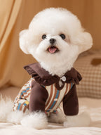 White dog wearing a brown and tan striped jumpsuit with a ruffled collar.