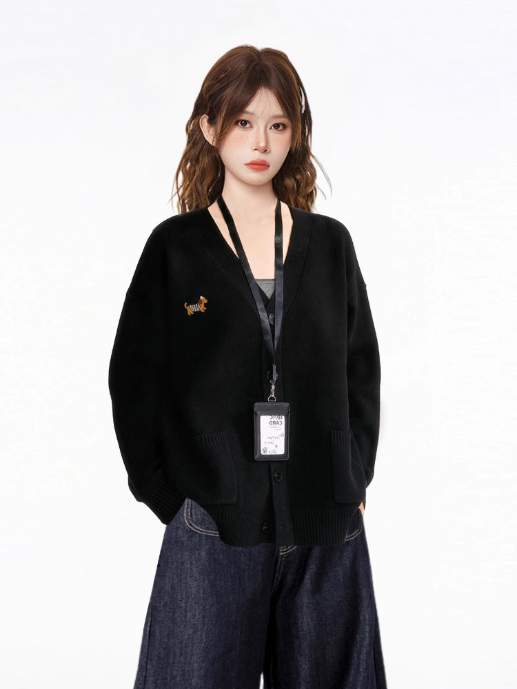 Close-up of a model wearing a black V-neck knit cardigan with an embroidered dachshund detail, a black tank top, and dark wash wide-leg jeans, with an ID badge holder around her neck.