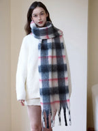 Full body shot of a woman wearing a cream-colored sweater and a long plaid scarf.