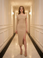 woman standing in a hallway wearing a beige asymmetrical ribbed knit midi dress with a high slit