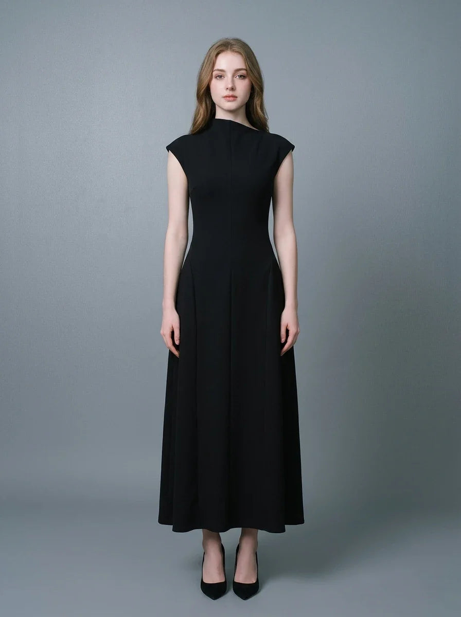 Woman in a black mock neck cap sleeve A-line dress standing against a grey background.