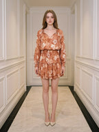 Woman standing in a hallway wearing a floral print mini dress with long sleeves and a V-neck.