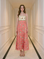 Woman in a coral A-line midi dress with spaghetti straps and a square neckline, standing in a hallway.