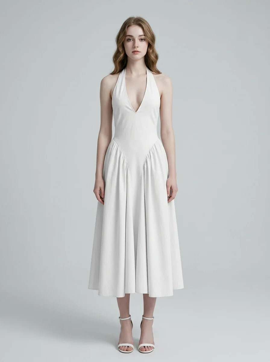 Woman wearing a white halter neck midi dress with a deep V-neckline and a full skirt, standing against a light grey background.