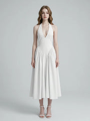 Woman wearing a white halter neck midi dress with a deep V-neckline and a full skirt, standing against a light grey background.