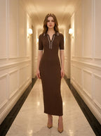 Woman standing in a hallway wearing a brown ribbed knit dress with white trim on the collar and sleeves, and nude high heels.