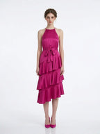Woman wearing a fuchsia satin halter tiered midi dress with a self-tie belt.