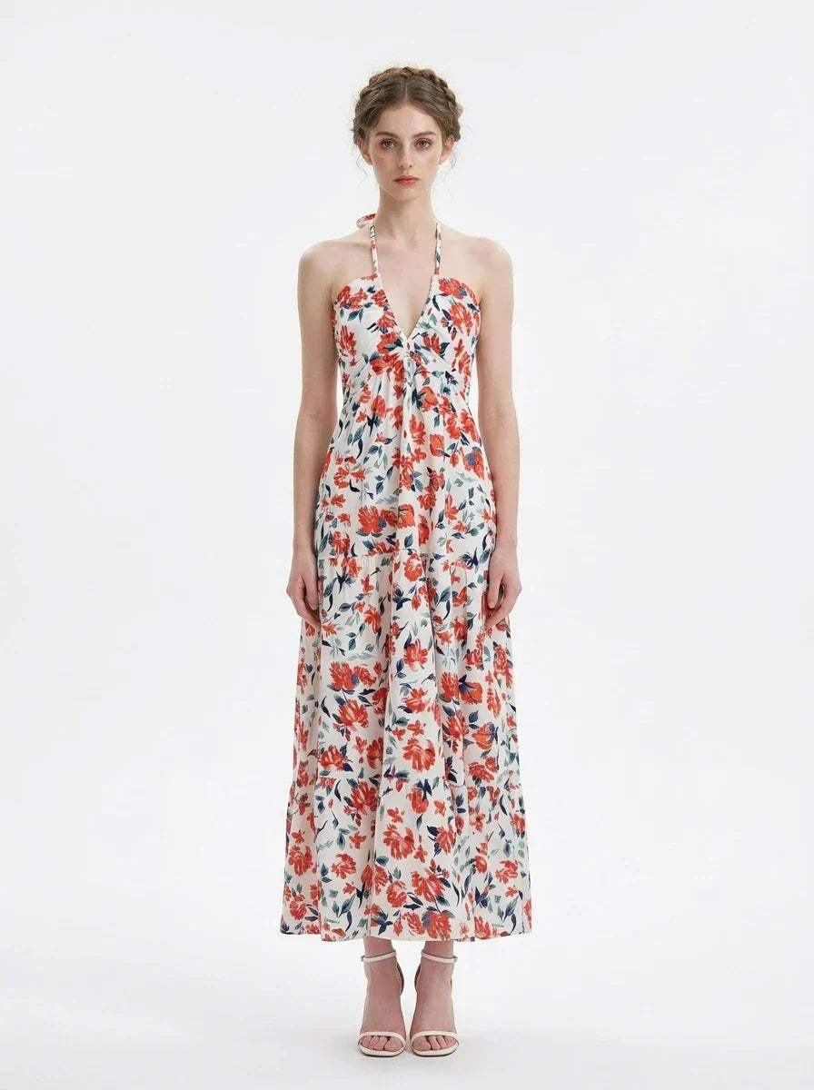 Woman wearing a white floral print maxi dress with a halter neckline and tiered skirt, standing against a white background.