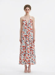 Woman wearing a white floral print maxi dress with a halter neckline and tiered skirt, standing against a white background.