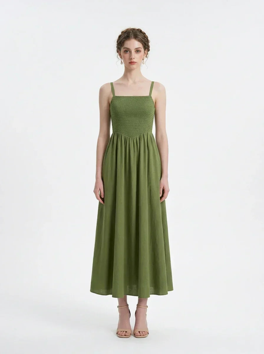 Woman wearing a green linen midi dress with a smocked bodice and square neckline, standing against a white background.