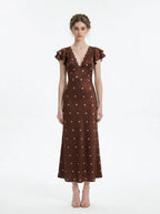 Woman wearing a brown polka dot midi dress with ruffled sleeves and a v-neckline, standing against a white background.