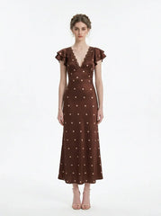 Woman wearing a brown polka dot midi dress with ruffled sleeves and a v-neckline, standing against a white background.