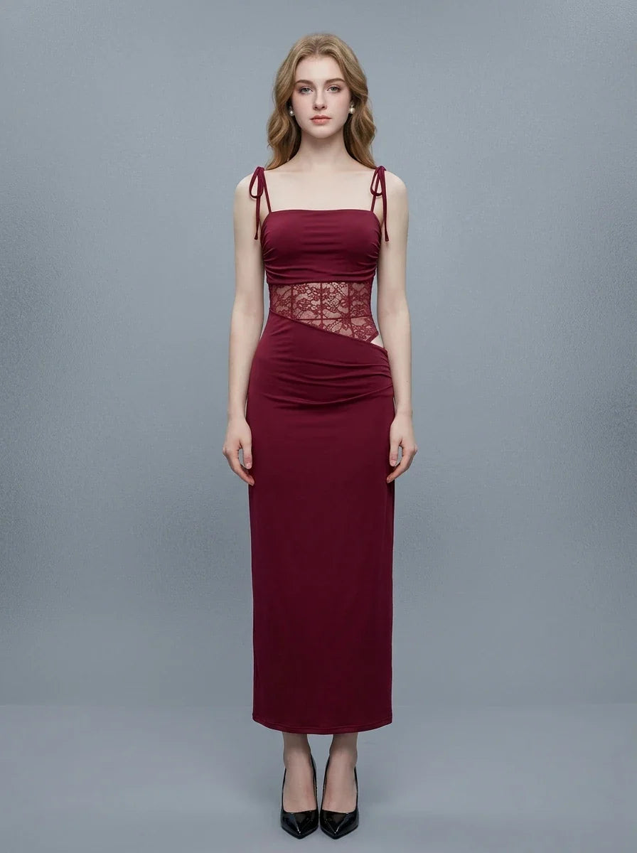 Woman wearing a long, burgundy slip dress with lace waist detailing, standing against a gray background.