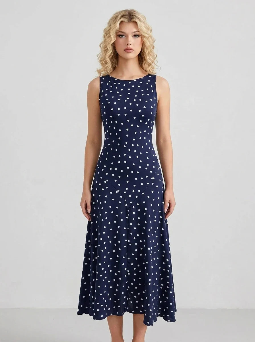 Woman wearing a navy blue sleeveless midi dress with white polka dots, standing and facing forward.