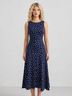 Woman wearing a navy blue sleeveless midi dress with white polka dots, standing and facing forward.