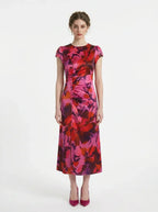 Woman wearing a pink and red floral print satin midi dress with short sleeves and ruched detailing, standing against a white background.