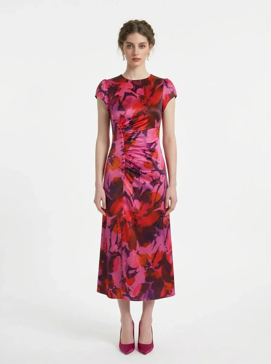 Woman wearing a pink and red floral print satin midi dress with short sleeves and ruched detailing, standing against a white background.