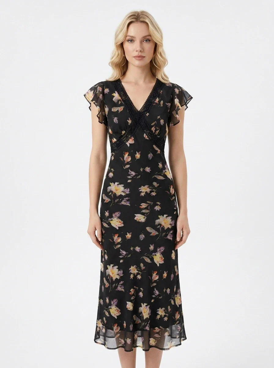 Woman wearing a black floral print midi dress with a v-neckline and short ruffled sleeves.