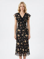 Woman wearing a black floral print midi dress with a v-neckline and short ruffled sleeves.