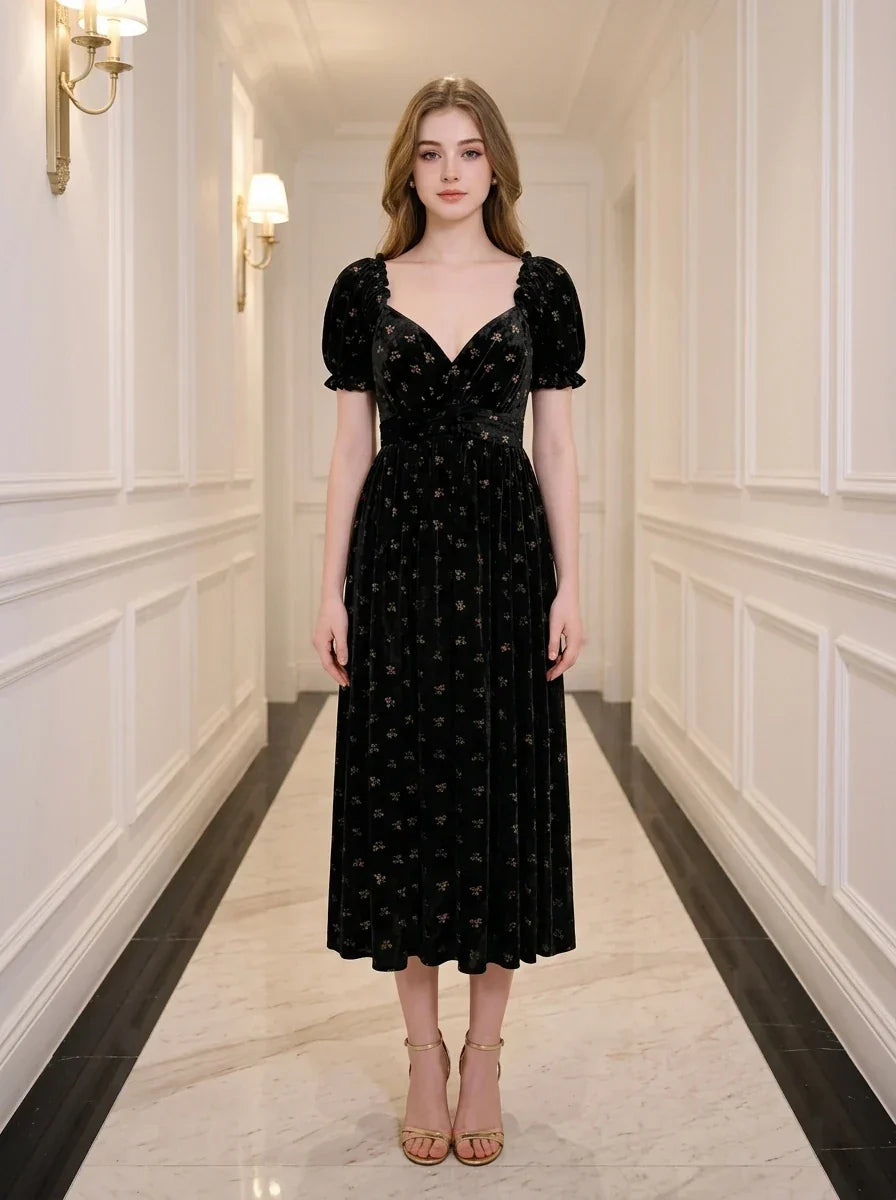 A woman stands in a hallway wearing a black velvet midi dress with a floral print.