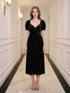A woman stands in a hallway wearing a black velvet midi dress with a floral print.