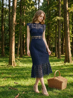 Woman in a navy blue lace mermaid dress with a high neck and cap sleeves, standing in a forest with a picnic basket.