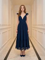 Woman standing in a hallway wearing a navy blue midi dress with ruffle sleeves and a deep V-neckline.
