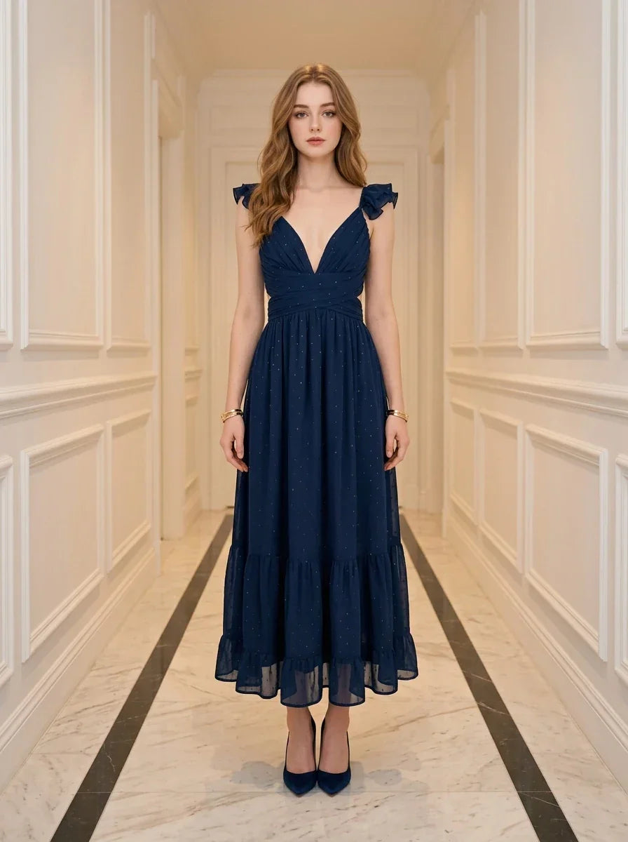 Woman standing in a hallway wearing a navy blue midi dress with ruffle sleeves and a deep V-neckline.