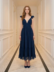 Woman standing in a hallway wearing a navy blue midi dress with ruffle sleeves and a deep V-neckline.