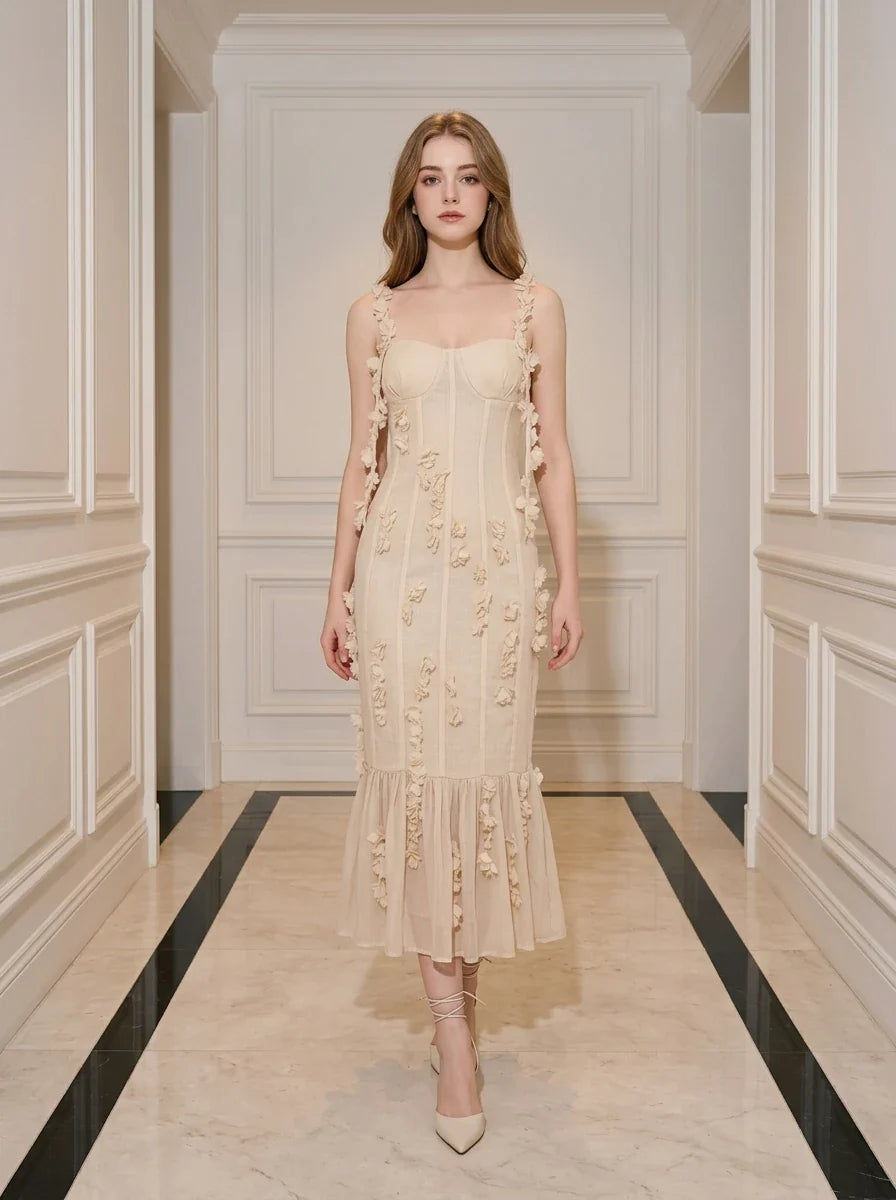 Woman wearing a cream-colored sleeveless midi dress with floral embellishments and a ruffled hem, standing in a hallway.