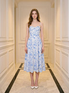 Woman wearing a blue and white floral print midi dress with spaghetti straps, standing in a hallway.