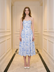 Woman wearing a blue and white floral print midi dress with spaghetti straps, standing in a hallway.
