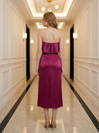 Back view of a woman wearing a strapless magenta satin midi dress with a high slit, standing in a hallway.