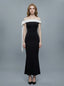 Woman wearing a black off-the-shoulder mermaid gown with a white sash and bow detail, standing against a grey background.