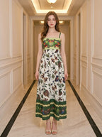 Woman standing in a hallway wearing a floral and bird print midi dress with spaghetti straps and a square neckline.